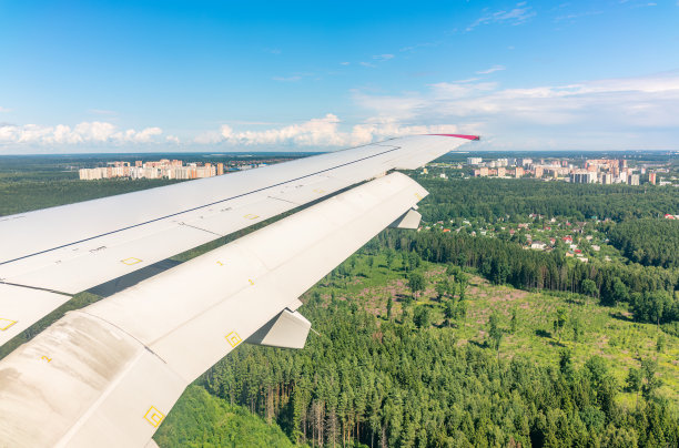 飞机机翼的视图，蓝天和绿色的土地在着陆。飞机窗口视图。图片下载