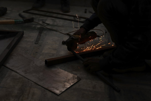 近景壮汉师傅手臂上没有戴手套，在车库车间用角磨机进行金属切割，蓝色和橙色的火花飞向四周图片下载