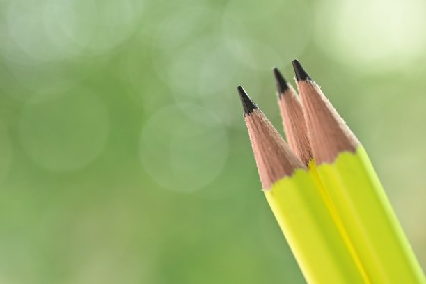 三个锐利的黄色木制铅笔在绿色模糊自然背景与散景图片下载