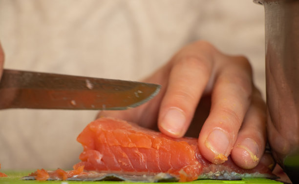 在厨房的餐桌上，一个女人用手把三文鱼切成沙拉图片下载