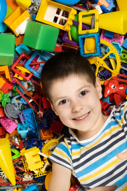 一个5岁男孩的肖像，背景是散落的玩具。童年快乐，玩具丰盈图片下载