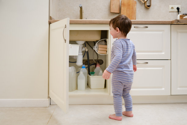 一个孩子正在厨房的洗涤槽下玩化学清洁产品。婴儿拿着装有洗涤剂的瓶子。两岁左右(一岁九个月)图片下载