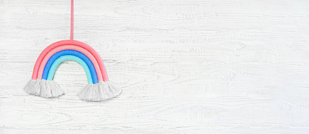 白色木墙上的软棉彩虹玩具。设计演示的婴儿模型，最小构成。为文本腾出空间。波西米亚儿童装饰。生日派对配饰。流苏花边针织。图片下载