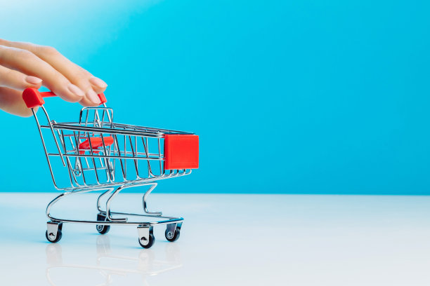 商务和电子商务的概念。站在蓝色背景下，用手指推着空的迷你购物车的特写镜头。侧视图。文本空间。图片下载