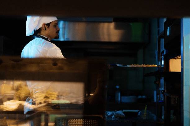 年轻的男厨师正在把披萨放进烤箱。图片下载