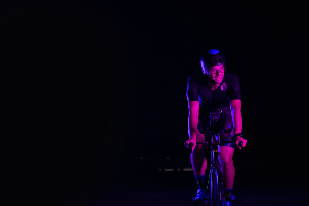 一个铁人三项运动员在漆黑的夜晚骑着自行车，强迫自己为马拉松做准备。自行车上的光线与黑暗的对比营造出一种戏剧性，突出了运动员的决心和毅力。图片下载