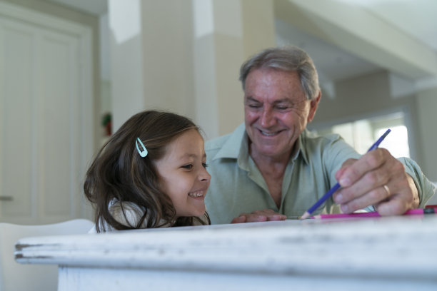 快乐的老人和孙女在家里的桌子上用彩色铅笔快乐地画画图片下载