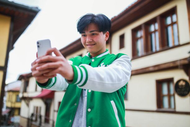 穿着大学夹克的年轻亚洲人在市中心观光。图片下载