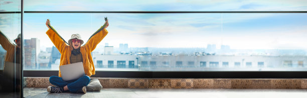 开朗的少女坐在露台上使用笔记本电脑，伸开双臂图片下载