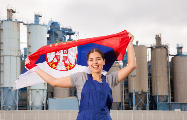 微笑的年轻女子手持塞尔维亚国旗站在工厂附近图片下载