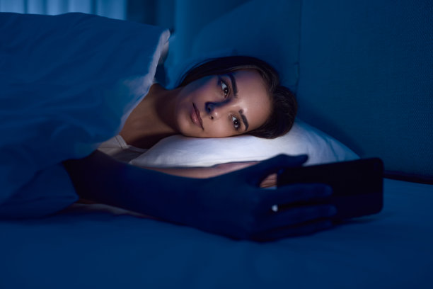 女人在黑暗的卧室里玩智能手机图片下载