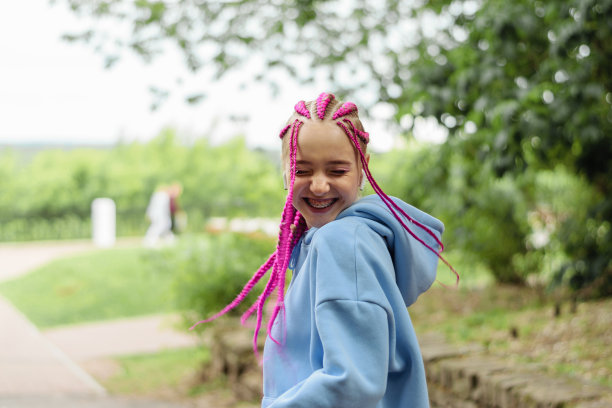 一个戴着粉色辫子的快乐白人少女在公园里戴着无线耳机的照片。Z世代风格，创意图片下载