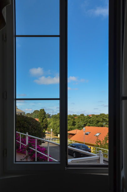 在一个阳光明媚的日子里，从一个敞开着大窗户的房间里，可以看到佩罗拉镇及其树木和绿色植被的壮丽景色。图片下载