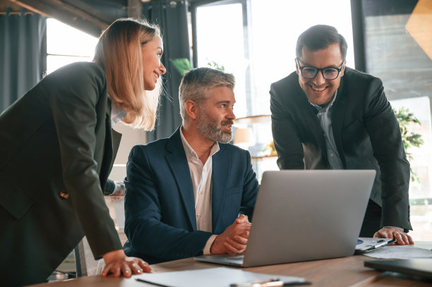 老人坐在笔记本电脑旁，员工在帮忙。一群商务人士正在现代化的办公室里工作图片下载