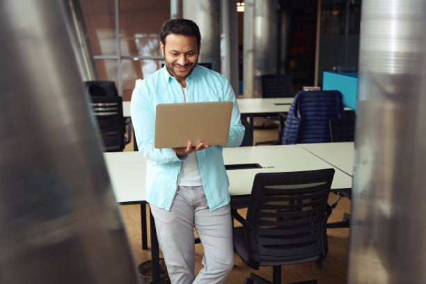 微笑的男人在办公室桌子旁使用笔记本电脑图片下载