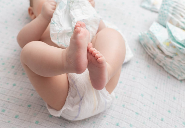 一个穿着尿布的婴儿躺在白色背景上玩一堆尿布。文本复制空间图片下载