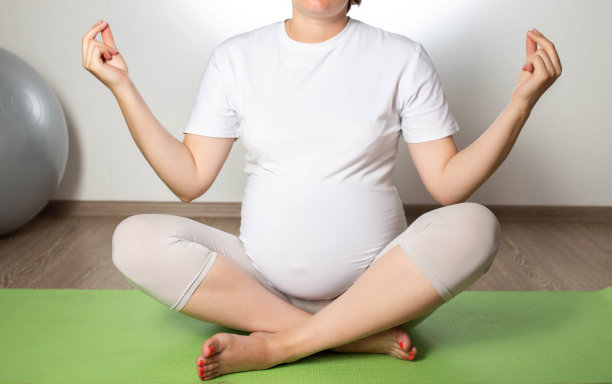 一个怀孕的女孩在一个白色背景的健身球上放松和冥想。女性健康。图片下载