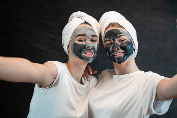 两名年轻女子身穿白色t恤，头上裹着毛巾，脸上戴着化妆用的黑色粘土面具图片下载