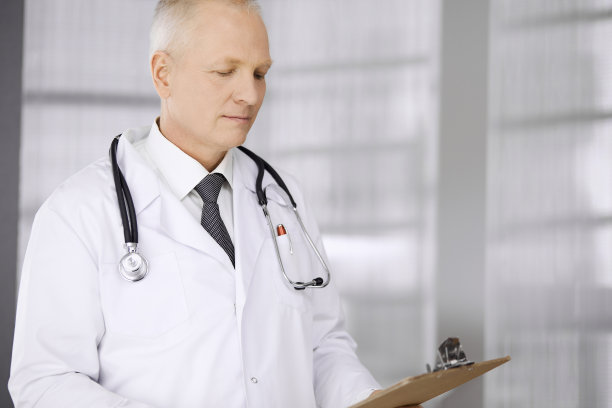 自信的老年医生在诊所站直并使用剪贴板。完善的医疗服务。医药保健理念图片下载