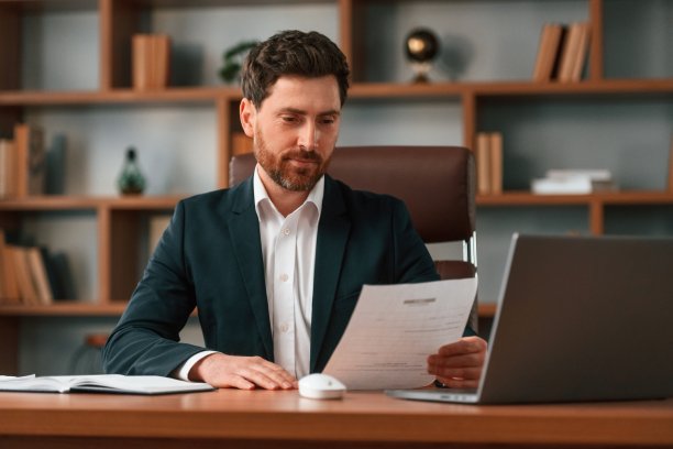 拿着笔记本电脑坐在桌子旁。穿着正装的商人正在室内工作图片下载