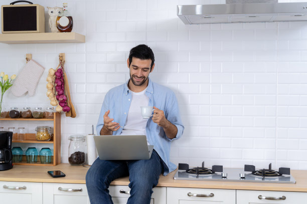 通过视频会议获得新知识。自学，网络学习理念。帅哥在厨房用笔记本电脑，在室内上网，图片下载