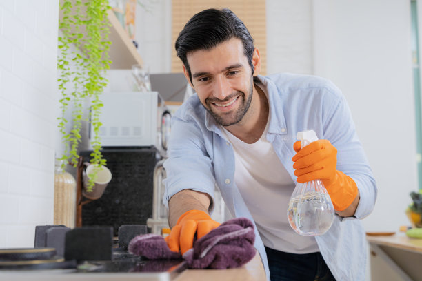 清理你的烦恼。一个年轻人在家里给厨房柜台消毒。年轻英俊的男人系着围裙，戴着防护手套擦拭水池图片下载