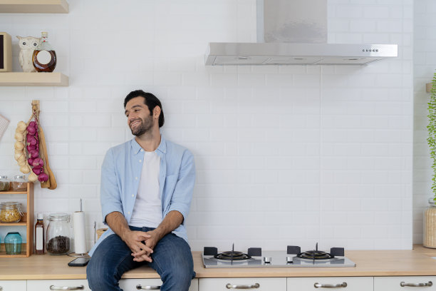 一个英俊的年轻人坐在厨房的柜台上看着窗外图片下载