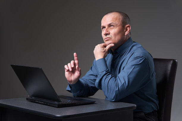 一个成熟的商人坐在他的办公桌前，用他的笔记本电脑图片下载