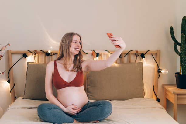 一名孕妇盘腿坐在床上，用手机拍了一张照片，然后上传到了社交媒体上图片下载