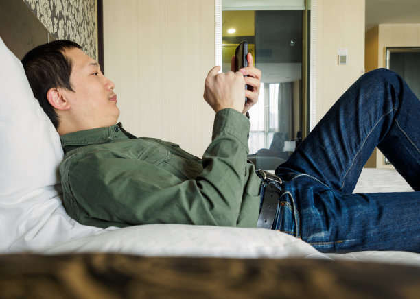 躺在酒店床上玩手机的男人图片下载