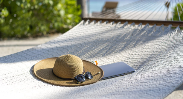 草帽、太阳镜和笔记本电脑躺在马尔代夫海滩的吊床上。远程工作和游牧的概念图片下载