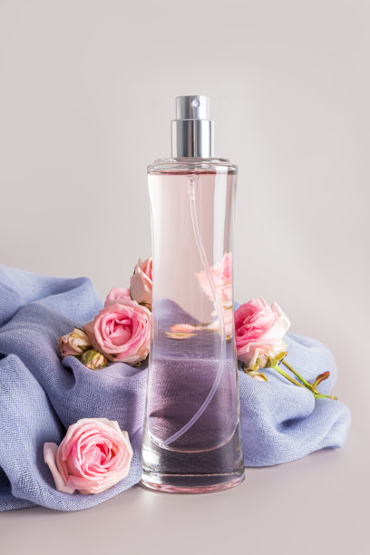 一瓶别致的女性香水，背景是一条带有精致活玫瑰的雪纺围巾。正面垂直视图。柔和的背景。图片下载