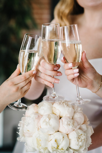 年轻的伴娘在酒店房间里碰杯喝香槟。欢快的女孩庆祝单身派对的特写照片。女性吃吐司配白葡萄酒。图片下载