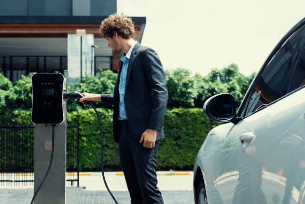 进步商人在公共停车汽车充电站为电动汽车充电。图片下载