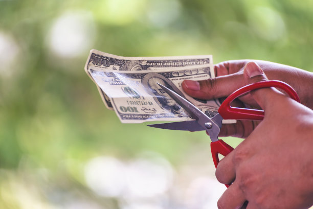 近距离手切钱美元钞票。女人手拿剪刀剪钱债。手持剪刀剪着100美元钞票。商人降低成本折扣图片下载