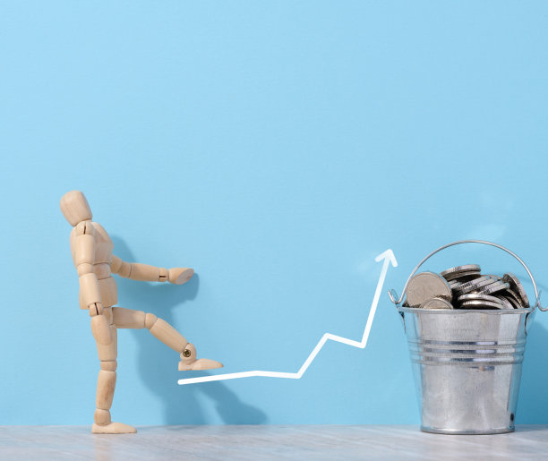 一个木制的人体模型和硬币放在一个小桶里，蓝色的背景，一个高收入的概念图片下载