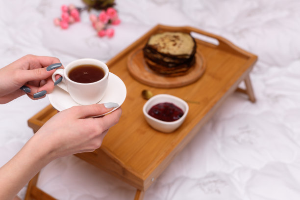 在床上喝茶。一个女孩手里的茶托上的一杯茶。图片下载
