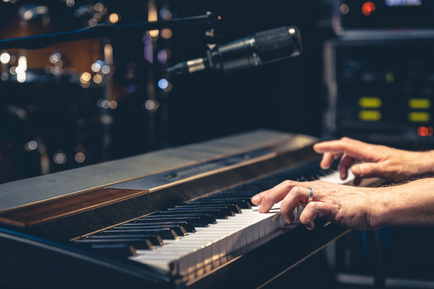 在一间音乐工作室黑暗的室内，一个男人的手在弹奏钢琴的琴键。图片下载