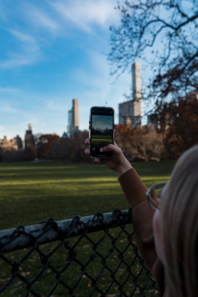 从中央公园俯瞰纽约。在纽约中心的公园里散步。这个女孩用手机拍照。图片下载
