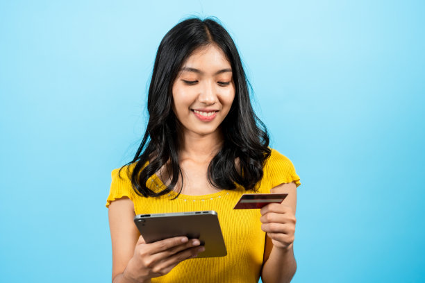 长头发的亚洲美女“肖像”，手持信用卡在笔记本电脑上用支付商品进行网上订购，蓝色背景的室内工作室与世隔绝。图片下载