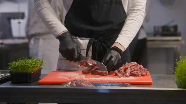 穿着围裙的厨师在菜板上切肉图片下载