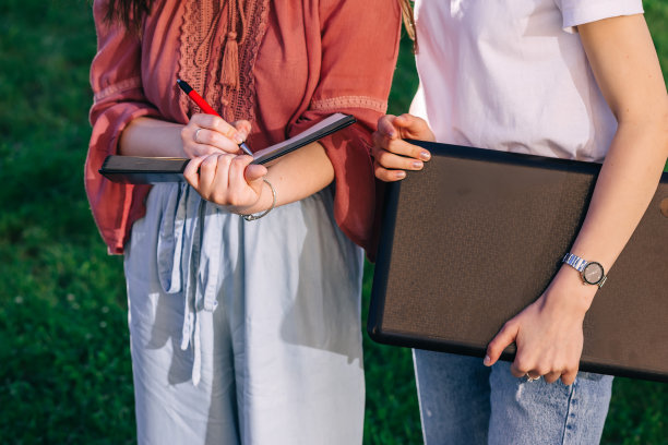 女孩们手里拿着一台电脑，在笔记本上做笔记。图片下载