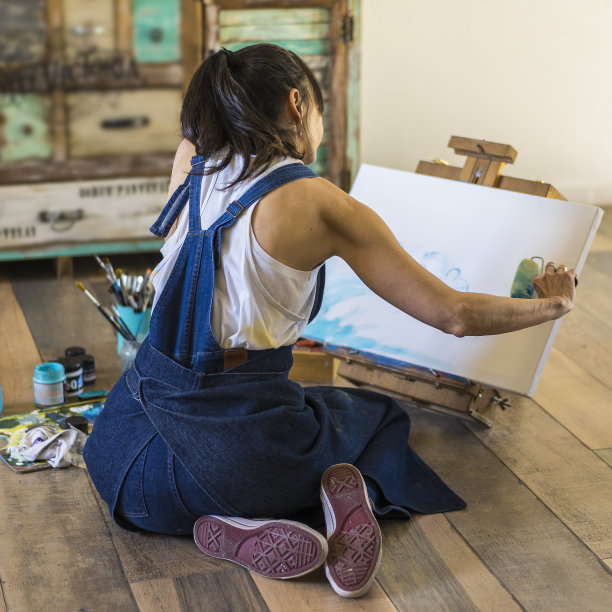 女画家在画布上画一幅蓝色的抽象画。有创意的女人在她的艺术工作室地板上工作。图片下载