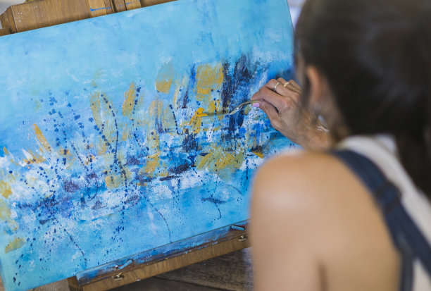 一个女人在画布上画一幅蓝色的抽象画的特写。图片下载