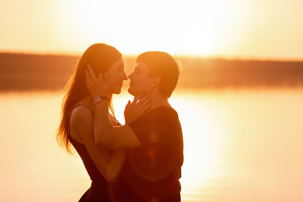 在橙色的夕阳下，一对恩爱夫妻的剪影特写。恋人拥抱，亲吻图片下载
