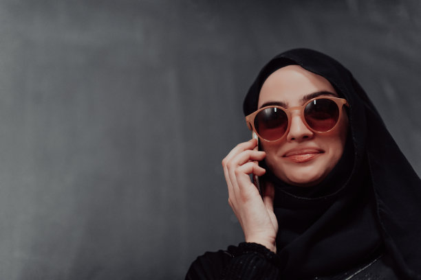 年轻的现代穆斯林女商人戴着头巾，在黑色黑板前使用智能手机图片下载