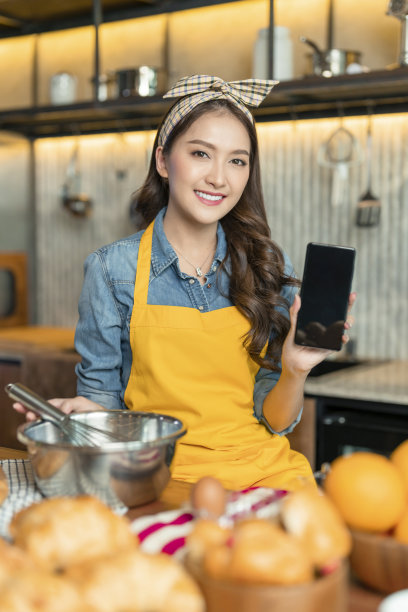 亚洲女厨师烘焙糕点面包。手持智能手机黑屏白屏显示食谱准备学习平板电脑在线社交媒体课程在家里的厨房，亚洲女性手使用智能手机图片下载