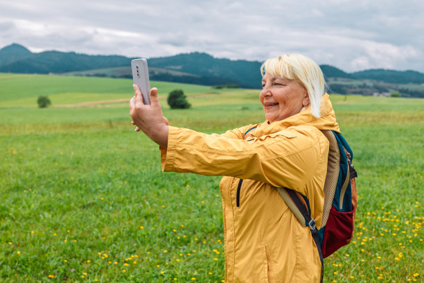 游客在山顶用智能手机拍照。戴着帽子，背包放在石头上的白人女人。旅行的概念。图片下载