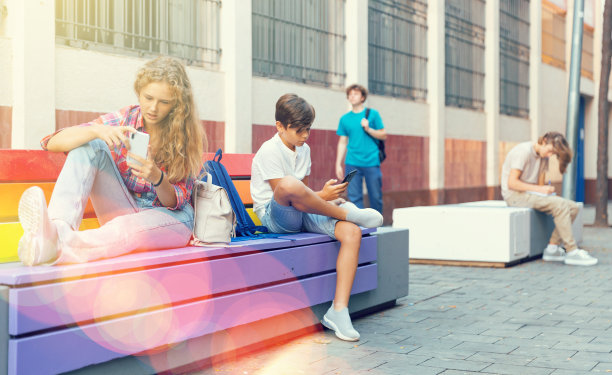 十几岁的男孩和女孩拿着智能手机坐在长椅上图片下载