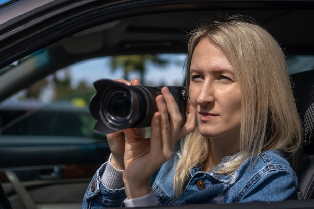 年轻的金发女郎坐在车里拍照。新闻的概念，侦探，报纸图片下载